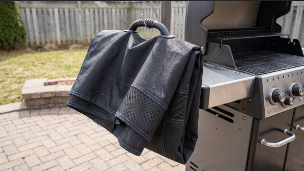 A folded Broil King cover hanging on a hook to dry beside the grill