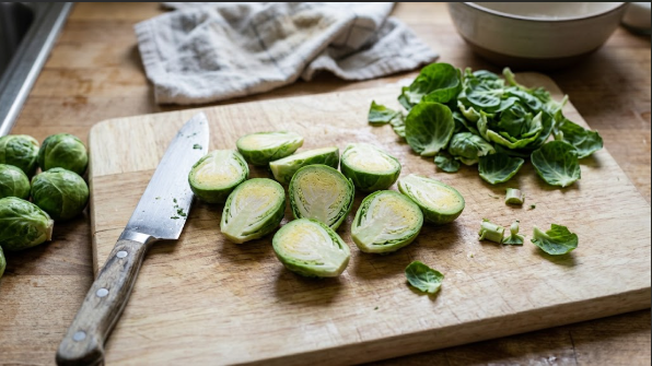 Halved Brussels sprouts on a cutting board, with loose leaves set aside