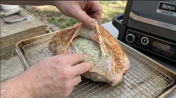Herb butter being spread under the skin of the turkey breast
