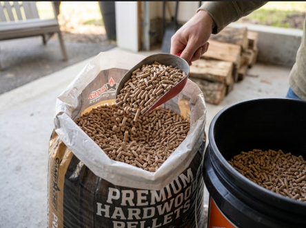 A hand scooping Camp Chef pellets from a bag into a bucket, showing even, dust-free pellets