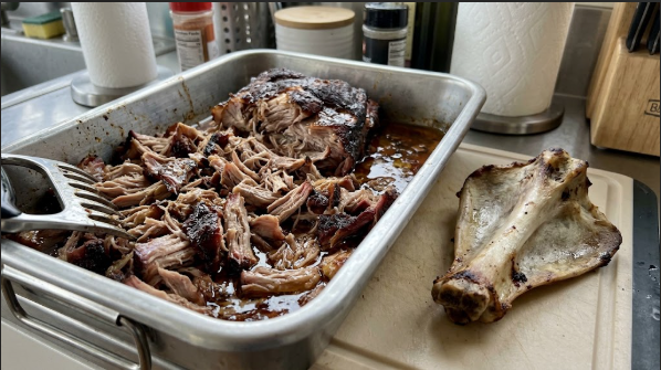 A shredded pork butt in a pan with the clean bone pulled out beside it