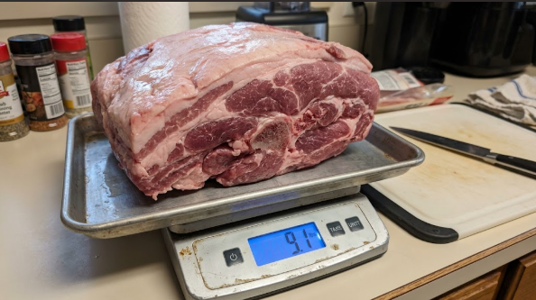 Raw bone-in Boston butt on a kitchen scale showing the weight before trimming