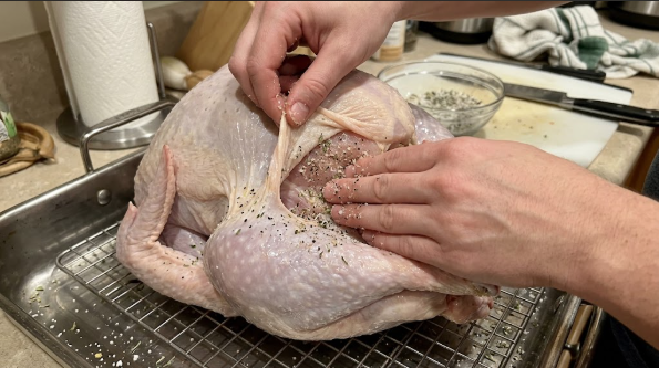 Raw turkey on a wire rack with salt mix being rubbed under the breast skin
