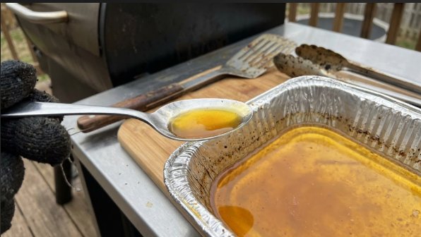 A spoon holding a drop of golden smoked butter next to the pan, showing the final color