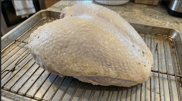 A bone-in turkey breast, skin side up, on a wire rack after dry brining, with dry, tight-looking skin
