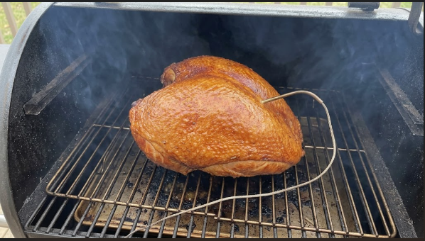 The turkey breast on the grate in the cook chamber, skin deep golden, with the thermometer probe and thin blue smoke visible
