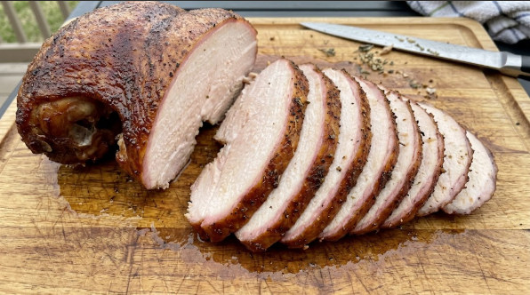 Carved turkey breast slices fanned on a cutting board, showing moist, pale pink-tinged meat and a smoke-colored edge