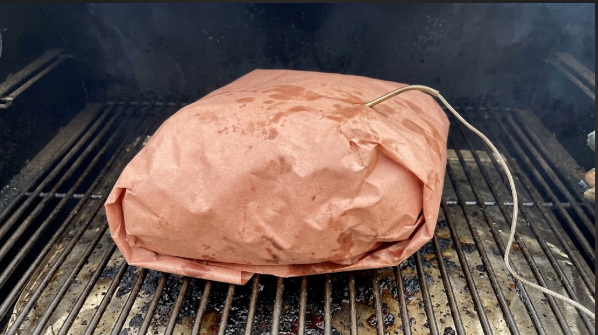 Pork butt wrapped in butcher paper on the smoker, probe visible in the thickest part