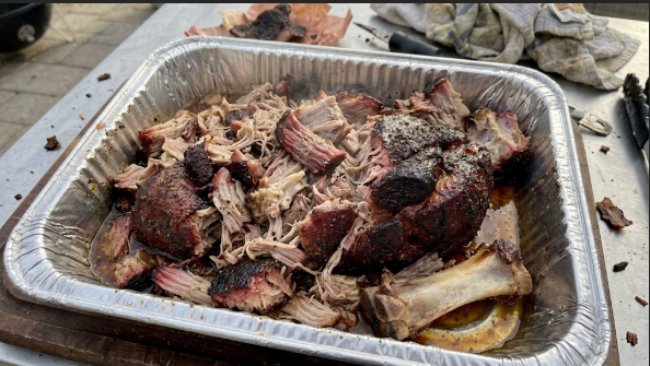 Finished pork butt pulled apart in a foil pan, showing juicy, shreddable meat and dark bark