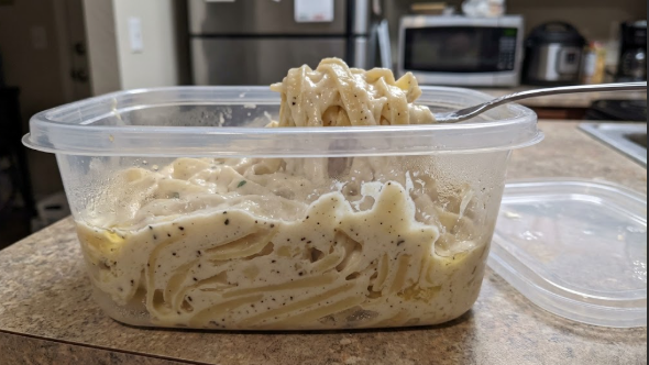 Cold leftover fettuccine Alfredo in a container, straight from the fridge, showing how thick and set it gets