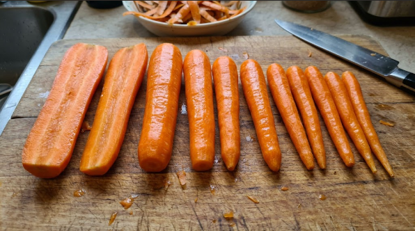 Washed and peeled carrots lined up on a cutting board, sorted by thickness, with a few thick ones halved lengthwise