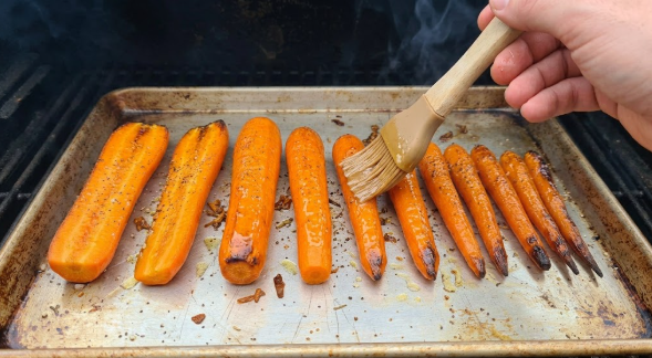  Carrots on the sheet pan being brushed with honey-butter glaze, with browned tips visible