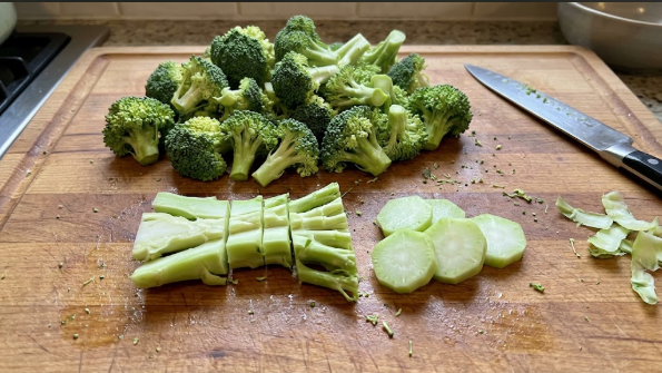 Broccoli crown cut into even florets, with split stems and peeled stem coins on a cutting board