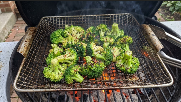 Seasoned broccoli florets in a grill basket over hot coals or burners