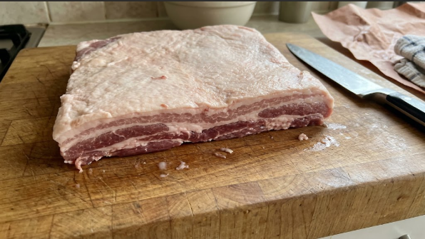 Raw skinless pork belly slab on a cutting board before trimming, showing fat and meat layers