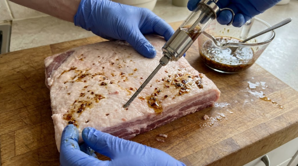 Meat injector inserted into pork belly in grid pattern with marinade visible