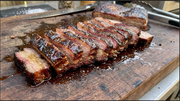 Finished sliced smoked pork belly on a cutting board, showing bark and juicy interior