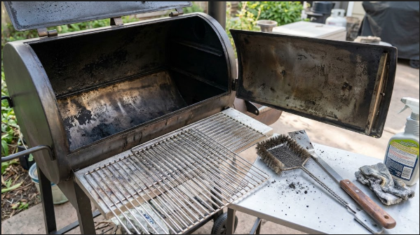 A clean smoker interior with racks pulled out and a brush and scraper laid beside them