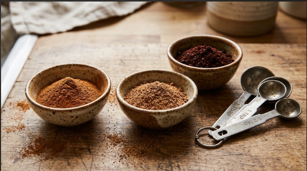Small bowls of ground cinnamon, nutmeg, and cloves next to a measuring spoon set