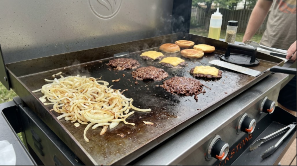 Smash burgers cooking on a Blackstone, with onions on a cooler zone