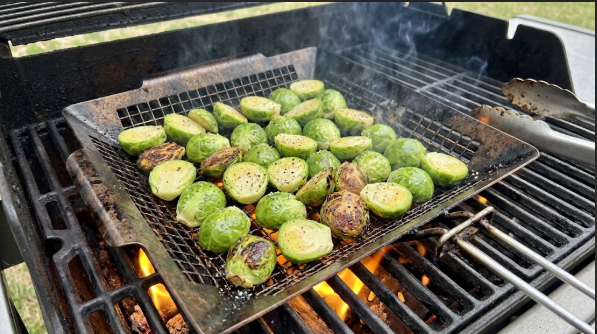 Halved sprouts spread cut side down in a hot grill basket on the direct side of the grill
