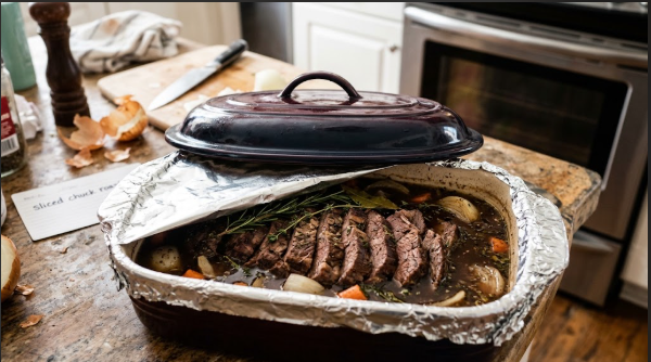 A covered baking dish of sliced chuck roast sitting in broth, ready to go into the oven