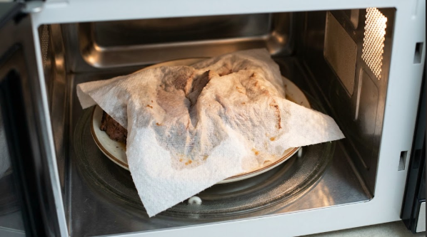 A plate of sliced chuck roast covered with a damp paper towel in the microwave