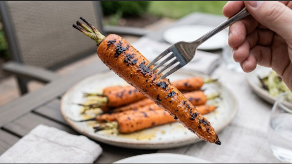 A fork piercing a finished carrot to show the tender center and charred exterior