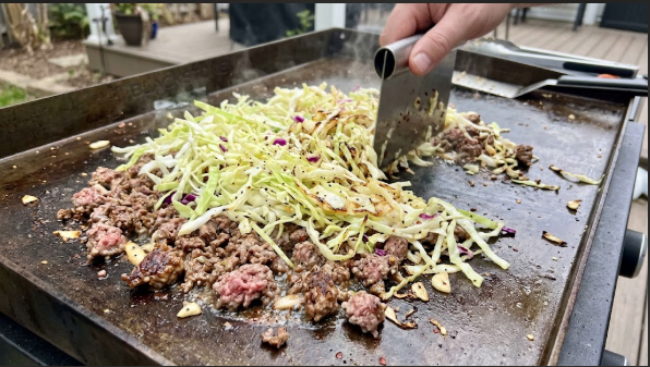 Ground beef and shredded cabbage sizzling together on a griddle