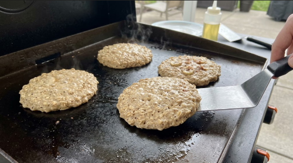 Banana oat pancakes on the griddle with bubbles forming, ready to flip