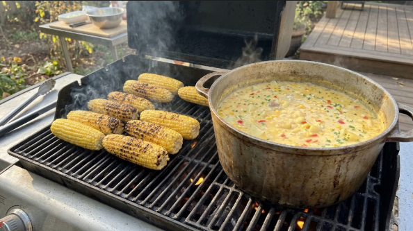 Corn on the grill with char spots, next to the pot of chowder