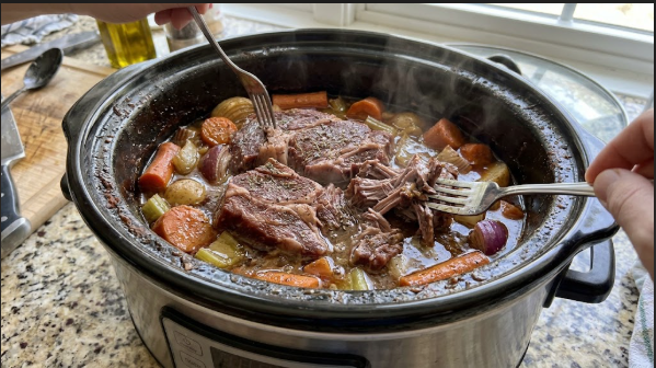 Shredded chuck roast being pulled apart with two forks directly in the crock
