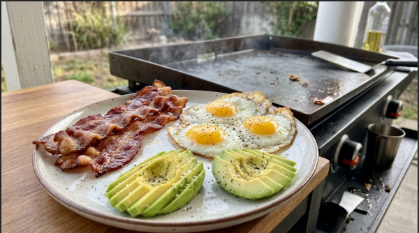 Blackstone breakfast plate with bacon, fried eggs, and sliced avocado