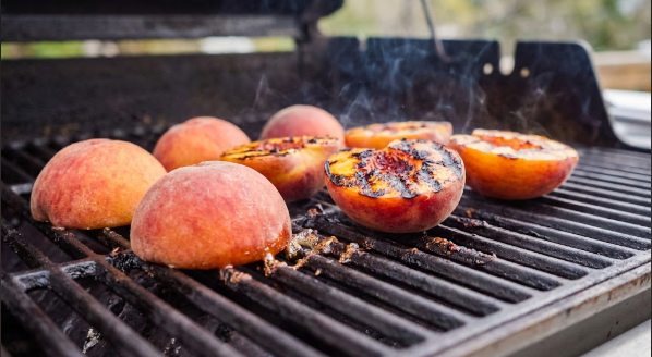 Peach halves cut-side down on the grill with dark grill marks