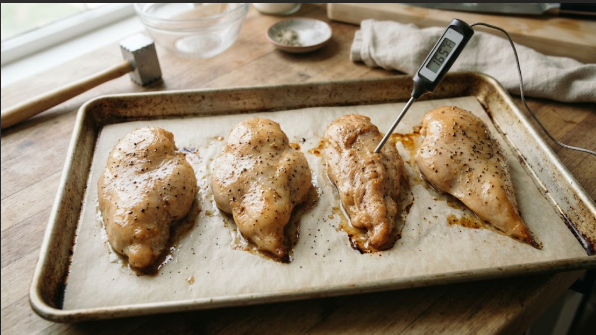 Finished baked chicken breasts on the sheet pan, golden and slightly glossy, with a thermometer in the thickest part showing the reading