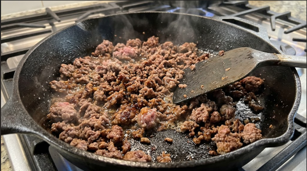 Lean ground beef browning in a cast iron skillet, showing deep brown crumbles and a spatula