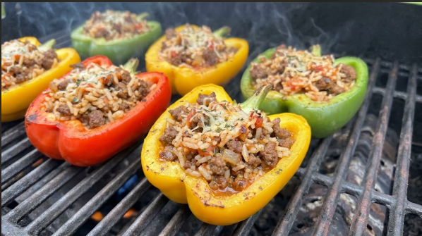 Halved bell peppers stuffed with beef and rice filling, sitting on grill grates over indirect heat