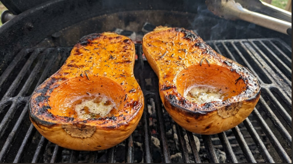 Smoked butternut squash halves with deeply caramelized edges, cut side up on the grate