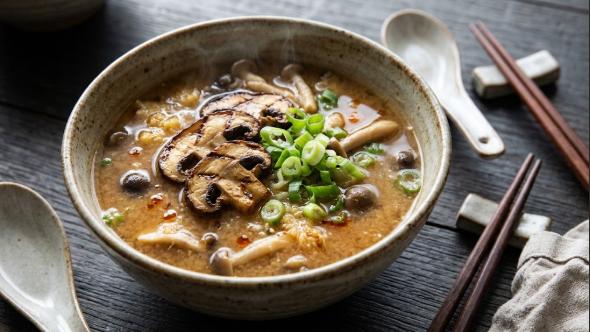 Bowl of miso ginger mushroom soup topped with sliced grilled mushrooms and green onion