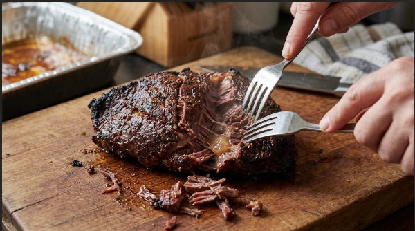 Fork-tender beef cheek being pulled apart on a cutting board