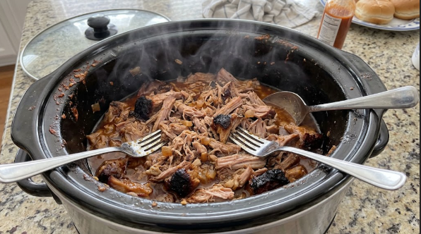Pulled pork shoulder shredded in the slow cooker, with visible steam and juices