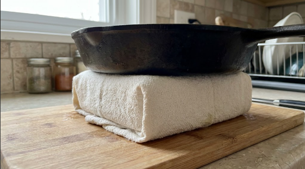 Block of extra-firm tofu wrapped in a towel with a cast iron skillet on top
