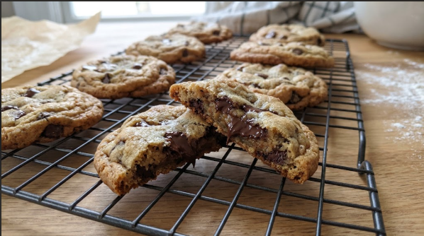 Finished cookies cooling on a wire rack with a split cookie showing a gooey center