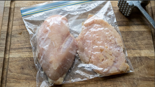 Raw chicken breast inside a zip bag, half pounded, showing the thick end next to the evened-out end