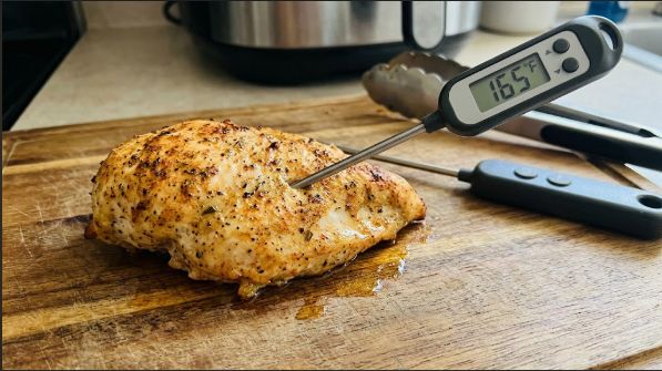 Finished air fryer chicken breast resting on a cutting board with a thermometer reading 165°F