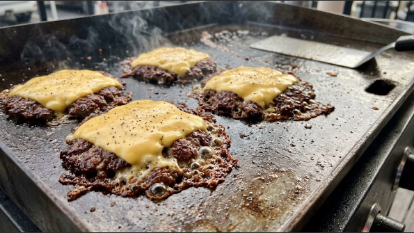 Smash burger patties on a griddle with crisp, lacy edges and melted cheese