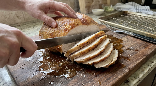 Carving the rested turkey breast into even slices, juices visible on the board