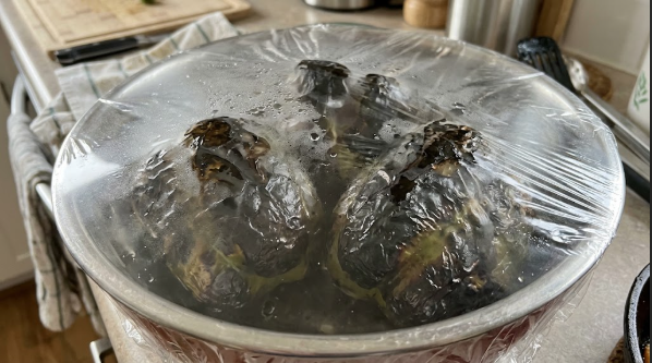 Blistered black bell peppers resting in a covered bowl