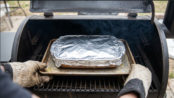 Casserole going onto the pellet grill grate under foil, on a sheet pan