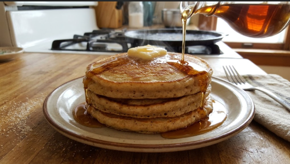 Finished stack of three pancakes with a pat of butter melting on top and syrup being poured